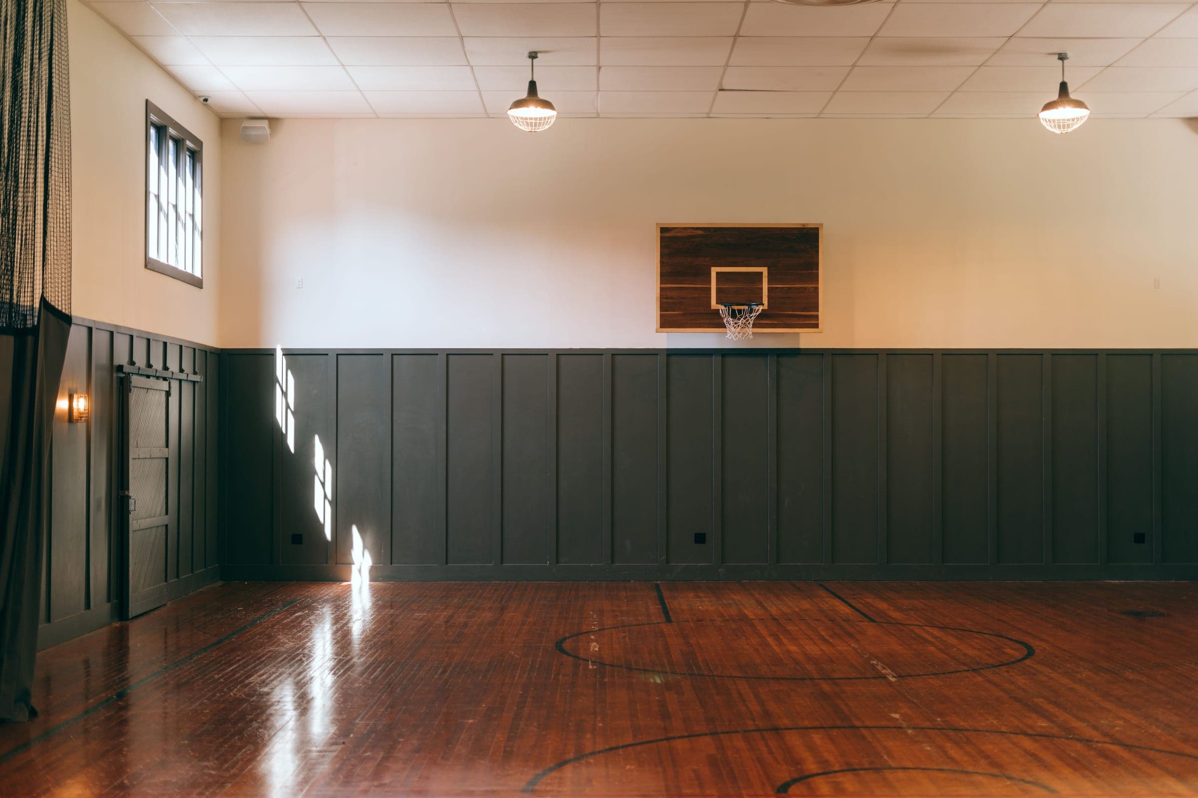 An empty hardwood basketball court under warm pendant lights